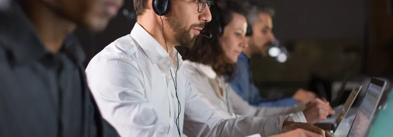 Technicians wearing headsets working a help desk at their computers